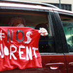A person holding a sign out the car window that says No Money No Rent.