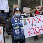Groups of people holding banners to tax the rich.